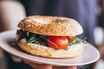 the waiter's hand holding a delicious and juicy stuffed bagel