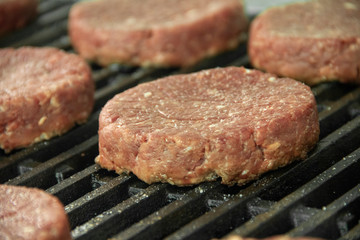 Close up of hamburger patties sitting on hot char broiler grill