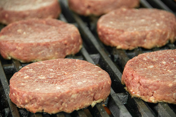 Close up of Raw hamburger patties sitting on hot char broiler grill