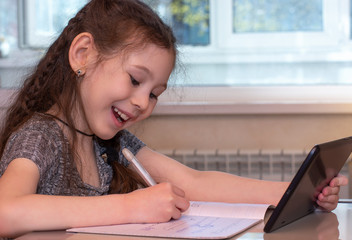 Schoolgirl typing at a tablet and doing homework. Distance home schooling. Online education