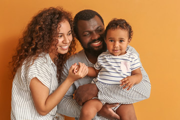 Happy African-American parents with cute baby on color background