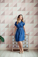 The image of a thinking young lady standing at the dresser . Looking to the side.