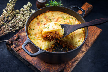 Traditional English shepherd pie offered as closeup in a Dutch oven on a wooden board