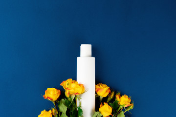 Top view of white cosmetic container with flowers on blue background, copy space