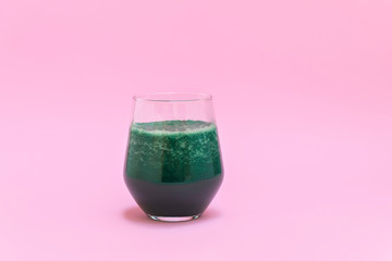 Glass of green fruit spirulina smoothie on pastel pink backgound