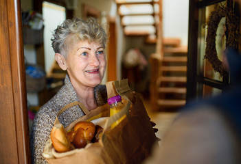 Unrecognizable courier delivering shopping to senior woman, corona virus and quarantine concept.