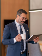 An office worker who actively uses social media, checking incoming data from his tablet during his standing coffee break