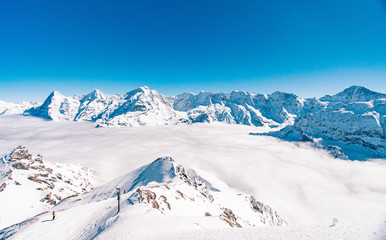 Vista do topo de uma estação de esqui na Suiça com o vale coberto de nuvens e o céu azul
