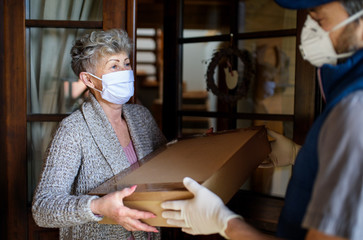 Courier with face mask delivering parcel to senior woman, corona virus and quarantine concept.