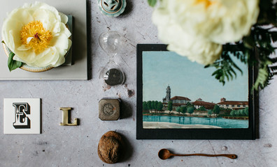 High angle view of peonies in bloom, original painting and a collection of various objects displayed on concrete table