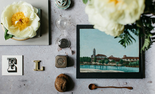 High angle view of peonies in bloom, original painting and a collection of various objects displayed on concrete table