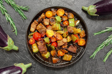 Fried vegetables with meat, vegetables, eggplant, herbs, rosemary on a black background.
