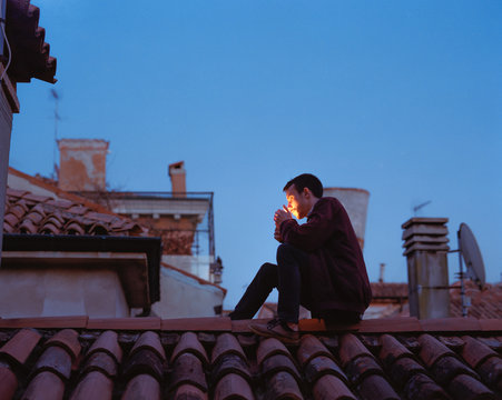 Young man sitting on roof with lighter