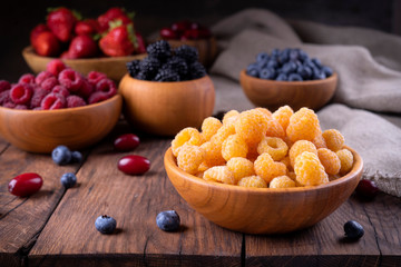 Yellow and red raspberries and other berries in bowls on a dark wooden 