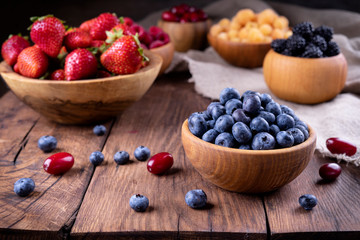 Blueberries and other berries in bowls on a dark wooden background.