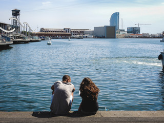 Obraz premium Chico y chica jóvenes sentados mirando al mar en el puerto de Barcelona
