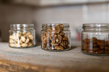 Almond, walnut and pistachio in a jars which standing on a white vintage table with a kitchen on background. Nuts is a healthy vegetarian protein and nutritious food. Nuts on rustic old wood.