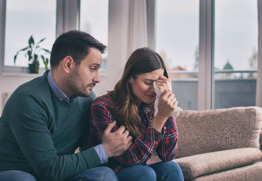 Man consoling sad girl at home with hug and his presence