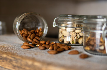 Almonds scattered on the white vintage table from a jar and with other nuts on background. Almond is a healthy vegetarian protein nutritious food. Almonds on rustic old wood.