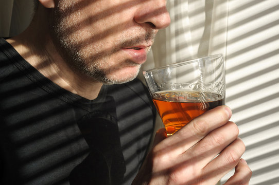 Man With Glass Of Whiskey Or Brandy At Home. Man Holding A Glass Of Whiskey Or Brandy By The Window. Sipping Whiskey Or Brandy.