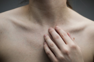 Woman with no face touching her hand to her neck and exposing her collar bones and décolletage; pale skin, freckles and moles