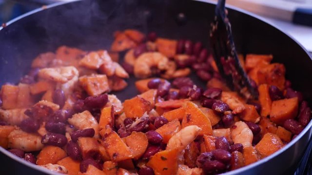 Healthy meal with shrimp, sweet potato , beans and spices being cooked in a pan .Mixing with a spatula.