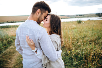Happy couple in love hugging, kissing and smiling against the sky in field. Hat in girl's hand