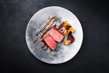  Barbecue dry aged wagyu roast beef natural sliced and offered with vegetable chips and herbs as top view on a modern design plate with copy space © HLPhoto