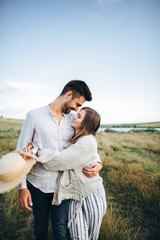 Happy couple in love hugging, kissing and smiling against the sky in field. Hat in girl's hand