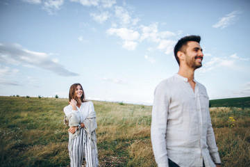 Happy couple in love hugging, kissing and smiling against the sky in field. Hat in girl's hand