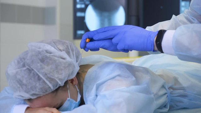 Doctor neurologist makes an injection to the female patient in the back along the spine. Healthcare and medicine concept
