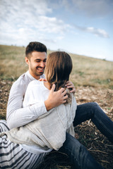 Lovely Сouple hugging, kissing and smiling against the sky seating on grass. Space for text