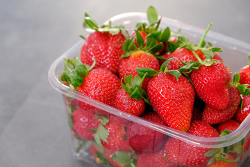 1 kg fresh strawberries in plastic box, on gray wooden background