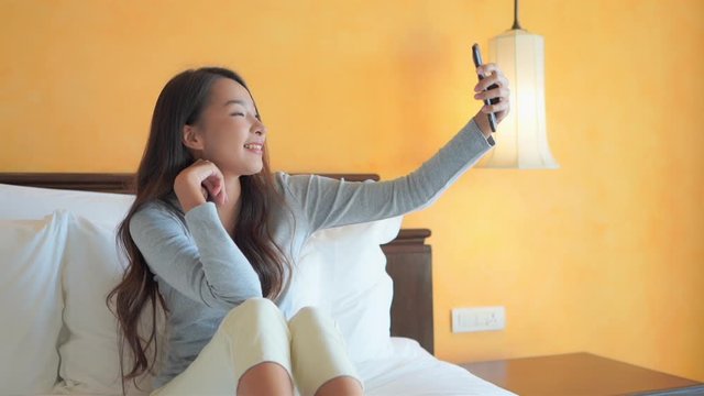 A young pretty social influencer Asian woman works on her selfie poses in her hotel room.