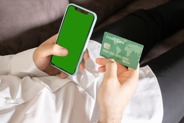 A black smartphone with green screen for chroma key compositing and a credit card in the hands of a man