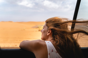 Young woman in car leaning out of window in Sahara Desert, Merzouga, Morocco