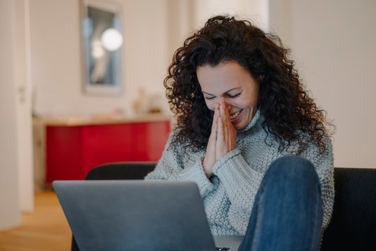 Woman sitting at home, using laptop, laughing