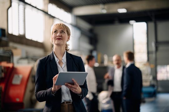 Portrait of a confident businesswoman with tablet in a factory with colleagues in backgound