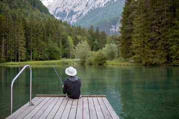 Fototapeta na wymiar Man fishing on the pier in a beautiful lake and forest with mountains.