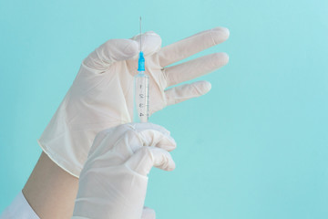 hands in white medical gloves hold syringe with liquid medicine inside, prepared for makig injection, vaccina from infection, protection from coronavirus pandemic, light blue background, copyspace