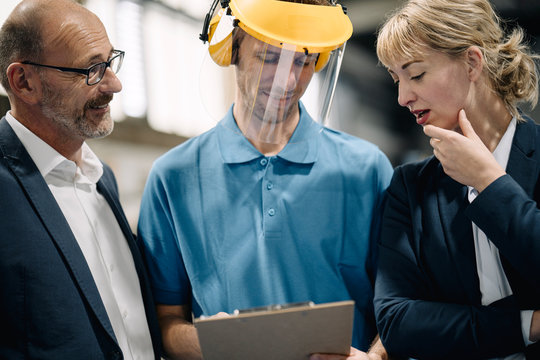 Business people and worker with clipboard talking in a factory