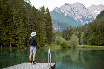 Man fishing on the pier in a beautiful lake and forest with mountains.