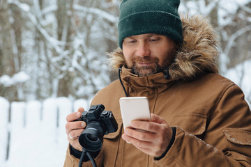 Portrait of bearded man looking with digital camera looking at cell phone in winter