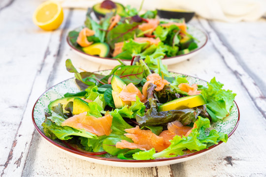 Two plates of ready-to-eat green salad with arugula,?Lollo?Rosso?lettuce, baby spinach, beetroot leaves, avocado, corn salad and salmon