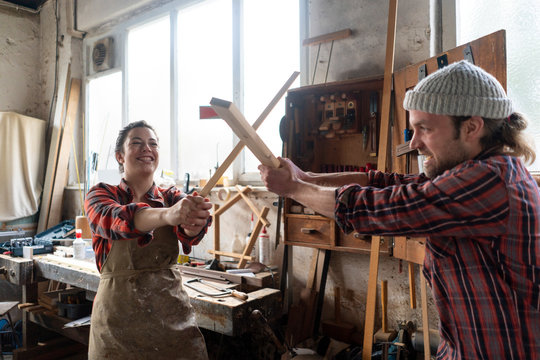 Playful craftswoman and craftsman fighting in their workshop