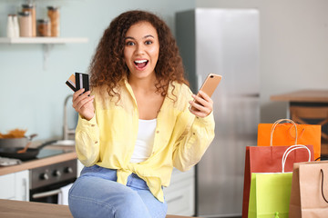 Happy woman with mobile phone, credit cards and shopping bags at home