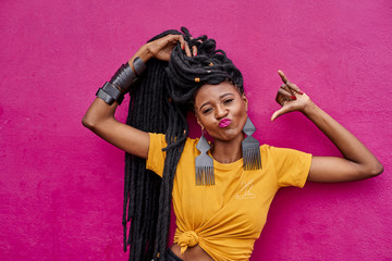 Portrait of woman with long dreadlocks making shaka sign in front of a pink wall
