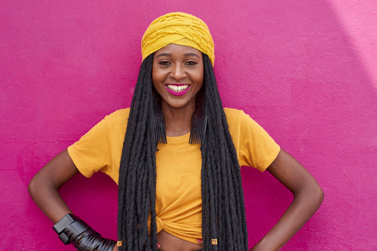 Portrait of woman with long dreadlocks in front of a pink wall