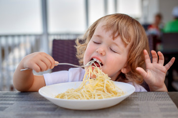 Adorable 2 years old little girl eating pasta and cutlet sitting in a cafe during her voyage, food and drink. Healthy eating for kids. Travel with young children