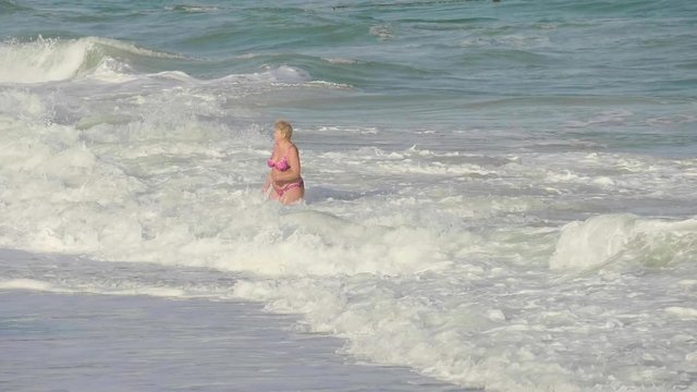 A well-nourished woman at the age of swimming in the sea with big waves.